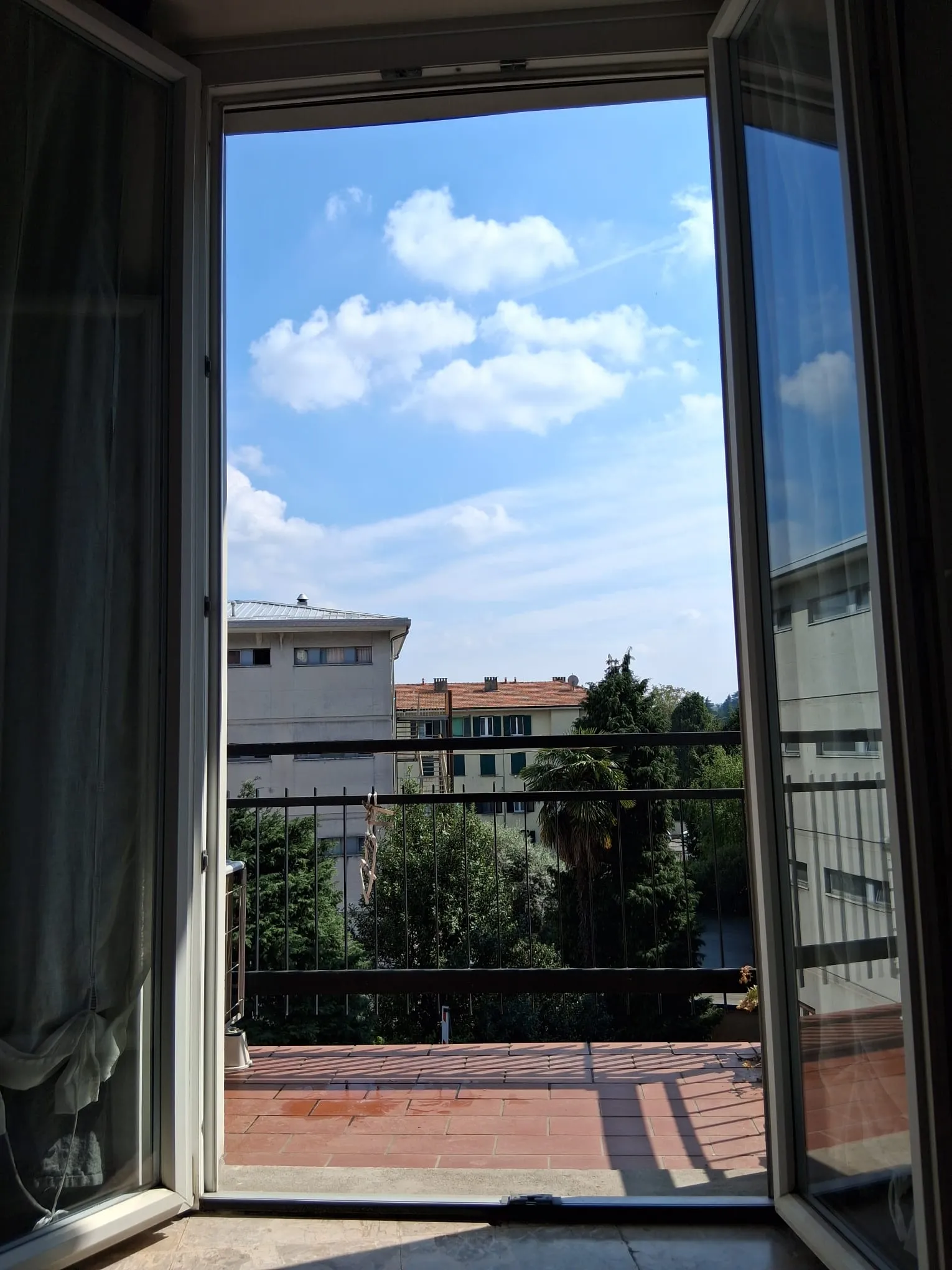 Der Blick von der Balkontür: Bäume, Dächer und blauer Himmel
