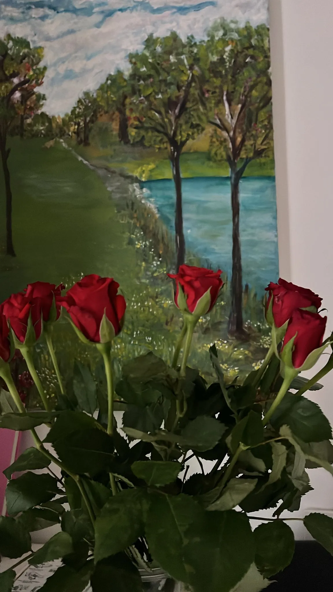 Rosas rojas delante de un cuadro con un lago y árboles